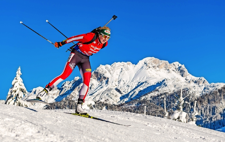 Biathlet beim Wettkampf auf schneebedecktem Berg mit blauer Himmel im Hintergrund.