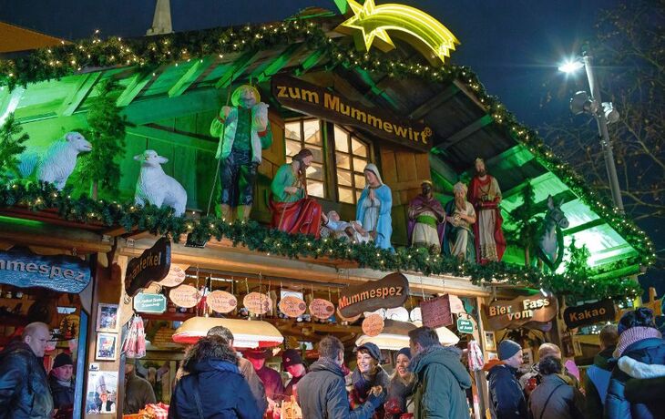 Weihnachtsmarkt mit Krippe, Holzhütte und Besuchern in festlicher Beleuchtung.