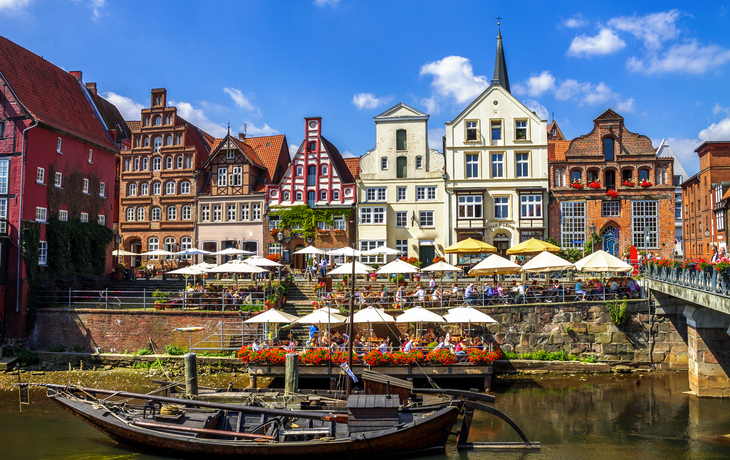 Fachwerkhäuser und ein traditionelles Boot an einem Flussufer bei Sonnenschein.