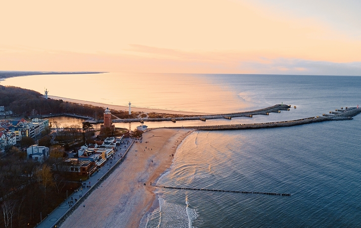 Luftaufnahme von Kolberg im Winter mit Küste und Leuchtturm bei Sonnenuntergang.