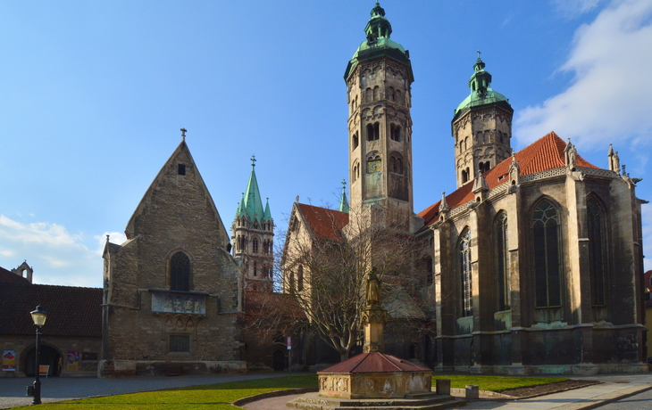 Historische Kirche mit Türmen und Brunnen auf sonnigem Platz.