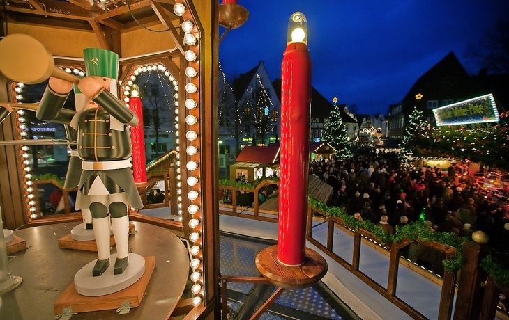 Weihnachtlich geschmückte Pyramide mit Figuren und Kerzen auf einem Weihnachtsmarkt abends.