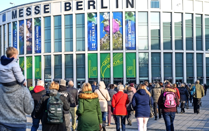 Menschen betreten die Messe Berlin mit Bannern der Grünen Woche am Gebäude.