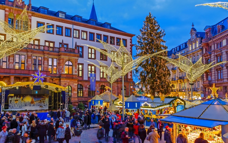 Weihnachtsmarkt mit festlichen Lichtern und geschmücktem Baum am Abend.