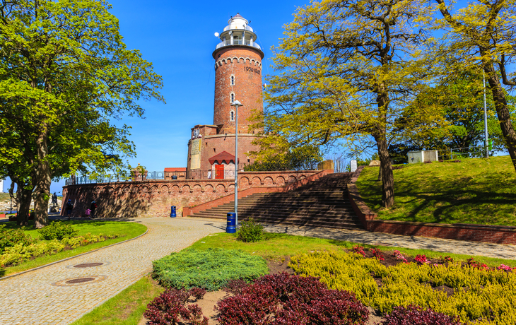 Leuchtturm von Kołobrzeg an der Ostsee, umgeben von Bäumen und einem Weg.