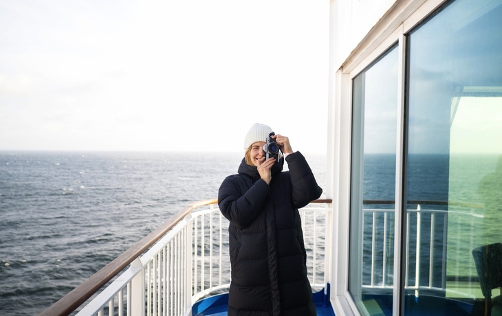 Frau mit Kamera auf einem Schiffsdeck vor dem Meer
