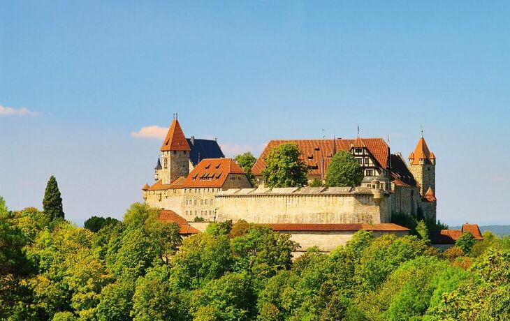 Burg Veste Coburg umgeben von grünen Bäumen und blauem Himmel.