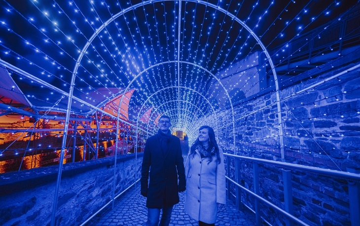 Personen spazieren durch einen Tunnel aus Lichterketten im Christmas Garden Koblenz.