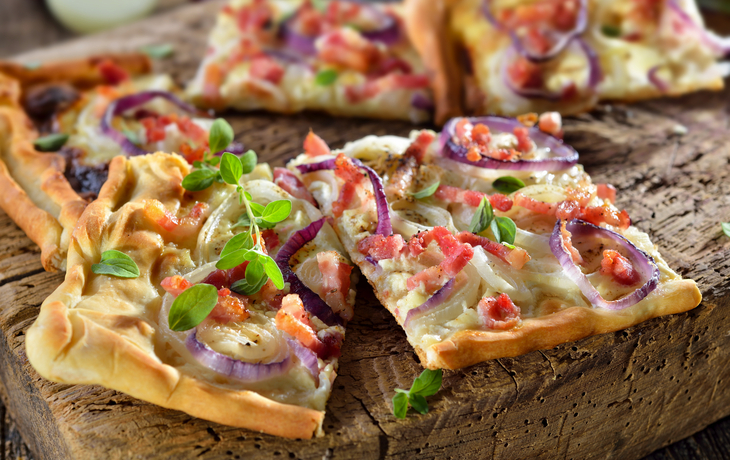 Flammkuchen mit Zwiebeln und Speck auf Holzbrett.