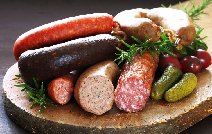 Verschiedene Wurstsorten auf einem rustikalen Holzbrett mit Kräutern und Gemüse.