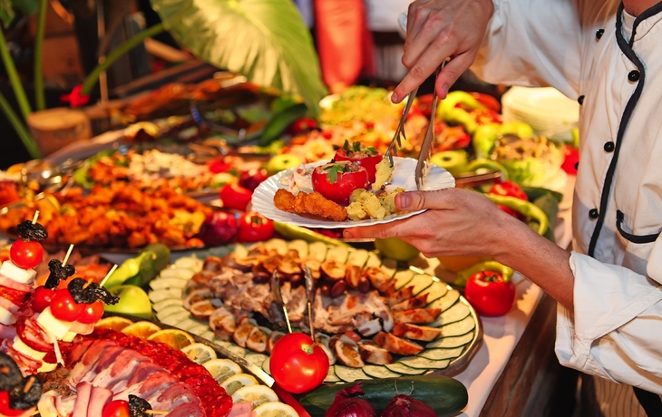 Ein Koch richtet einen Teller mit verschiedenen Speisen an einem Buffet an.