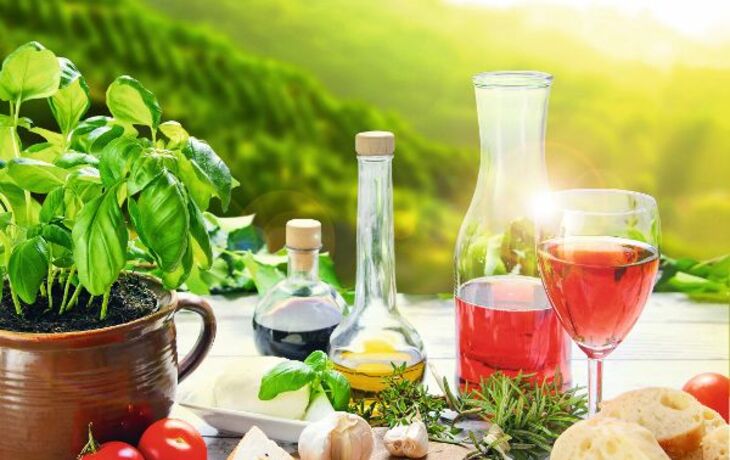 Käse, Wein, Tomaten, Basilikum und Brot auf einem Tisch mit Landschaft im Hintergrund.