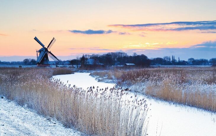 Windmühle am zugefrorenen Kanal bei Sonnenaufgang im winterlichen Holland.