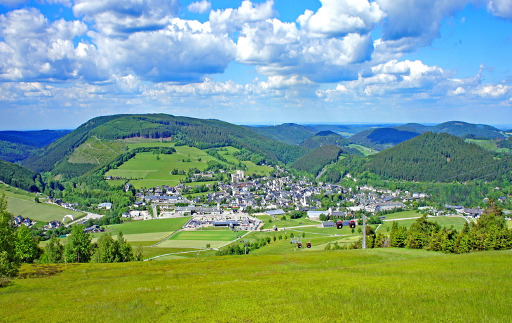 Panorama einer grünen Landschaft mit Hügeln und Wolken am Himmel.