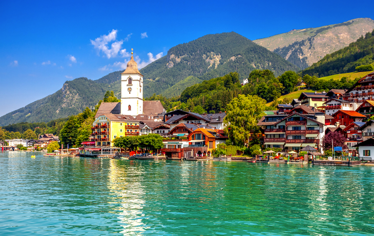 Stadt am See mit Kirche und Bergen im Hintergrund.