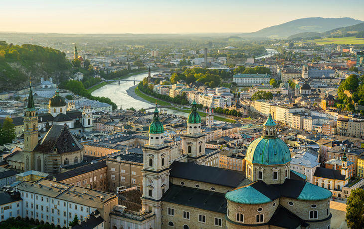 Stadtansicht von Salzburg mit Fluss und historischen Gebäuden im Abendlicht.