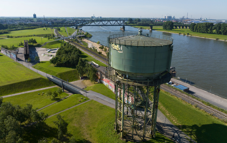 Luftaufnahme eines Wasserturms in Duisburg an einem Fluss mit umliegender Landschaft.