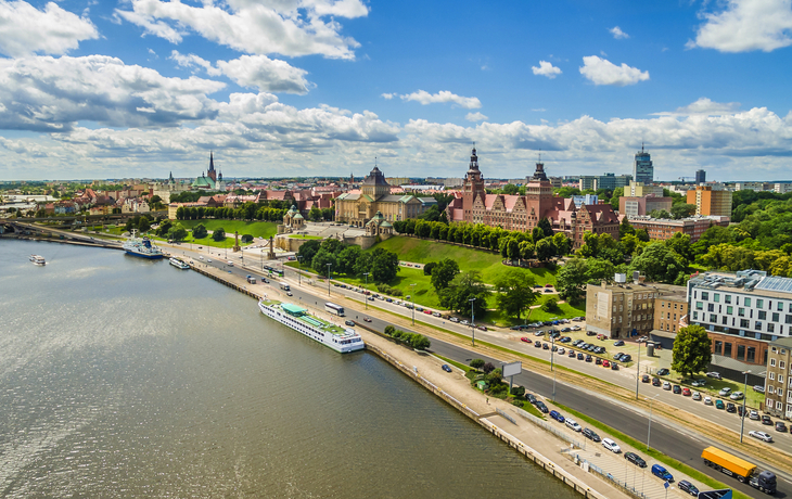 Stadtansicht mit Fluss, Promenade und historischen Gebäuden am Ufer.