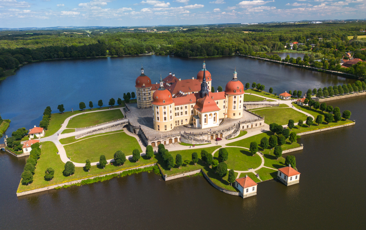 Schloss Moritzburg in Sachsen, umgeben von einem Teich, bei blauem Himmel im Frühling.