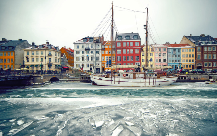 Ein Schiff im gefrorenen Wasser vor einer Reihe bunter Gebäude in einer alten europäischen Stadt.