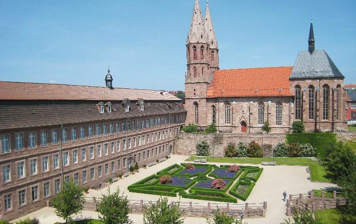 Historisches Gebäude mit zwei Kirchtürmen und gepflegter Gartenanlage.