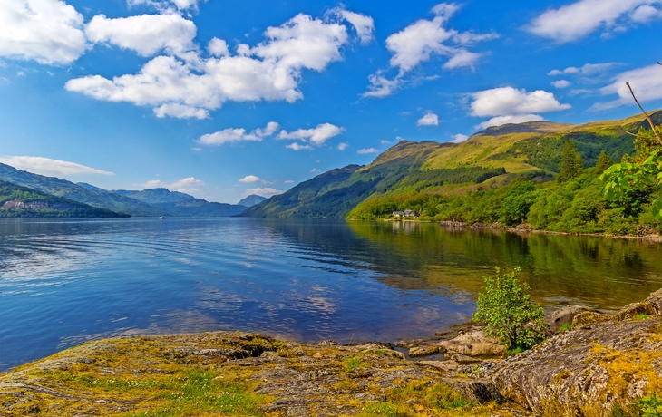 Blick auf Loch Lomond in Schottland mit Bergen und blauem Himmel im Hintergrund.