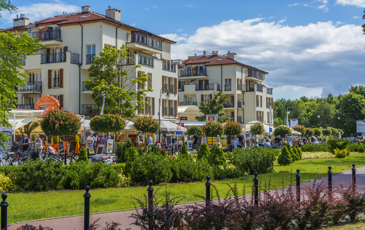 Promenade in Swinemünde mit Gebäuden und Grünflächen bei sonnigem Wetter.