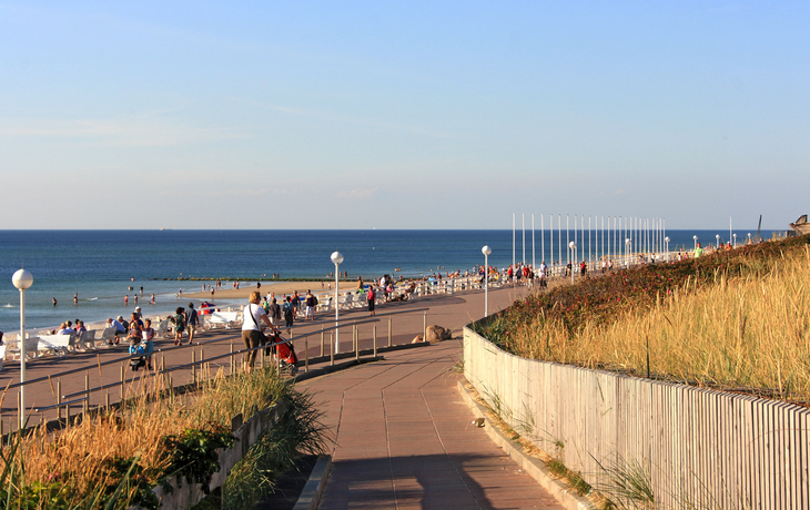 Promenade am Strand mit Spaziergängern und blauem Himmel im Hintergrund.