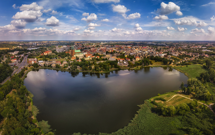 Stadtansicht mit See und grüner Landschaft unter blauem Himmel.