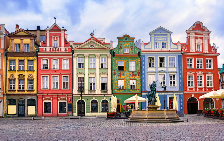 Bunte Renaissancefassaden am zentralen Marktplatz in Posen mit einer Brunnenskulptur im Vordergrund.
