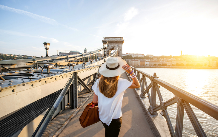 Frau mit Hut geht über eine Brücke bei Sonnenuntergang.