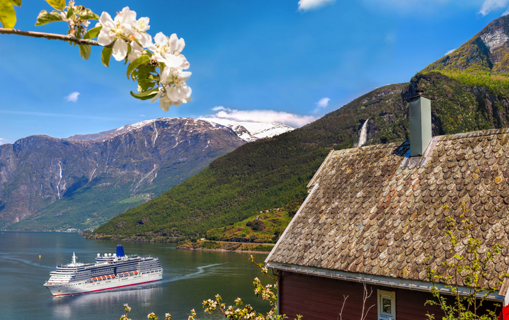 Rotes Haus und Kreuzfahrtschiff im Aurlandsfjord, Norwegen, umgeben von Bergen