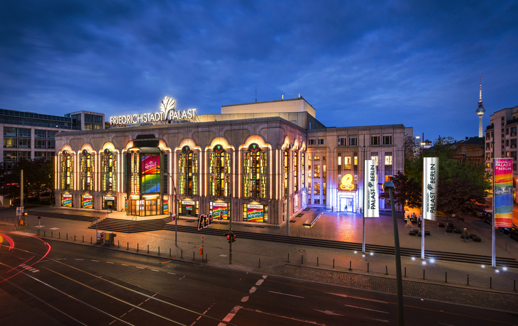 Außenansicht des beleuchteten Friedrichstadtpalasts in Berlin bei Dämmerung.