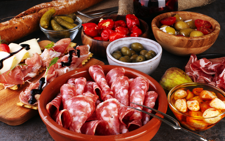 Verschiedene Antipasti auf Holzbrett mit Salami, Oliven, Brot und eingelegtem Gemüse.