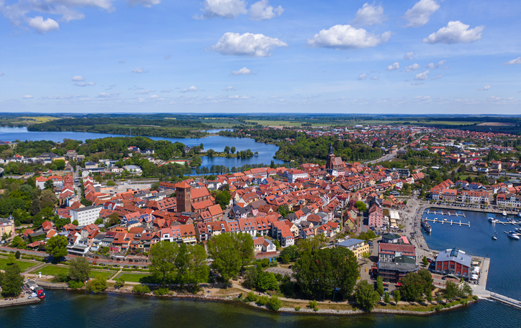 Luftaufnahme einer Stadt mit roten Dächern an einem Seeufer bei klarem Himmel.