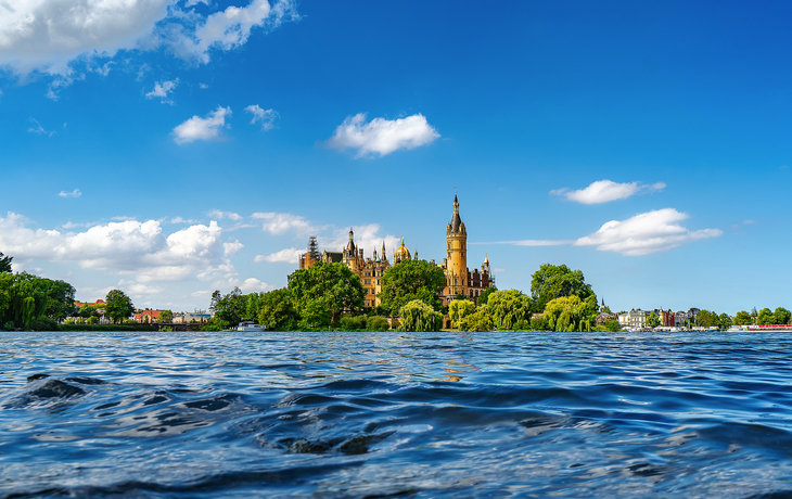 Schweriner Schloss im Sommer, von Wasser und Bäumen umgeben.