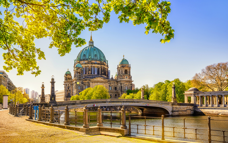 Berliner Dom im Sommer bei sonnigem Wetter, an der Spree gelegen, umgeben von grünen Bäumen.