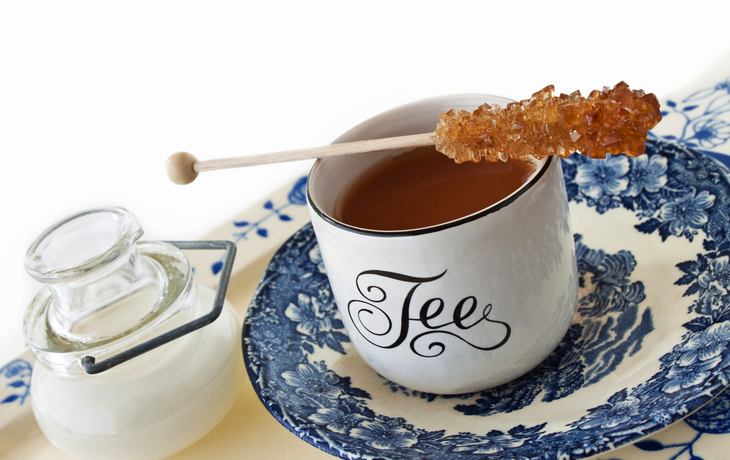 Tasse Tee mit Kandiszucker auf blau-weißem Geschirr, daneben Milchkanne.